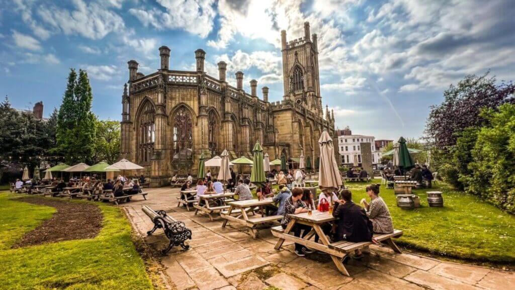 Patrons enjoying a sunny day at the unique outdoor seating area of the Bombed Out Church in Liverpool, a fun and historical city landmark.