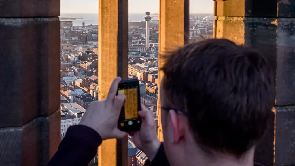 A visitor captures the stunning cityscape of Liverpool on their phone from the clock tower, showcasing a unique and fun perspective