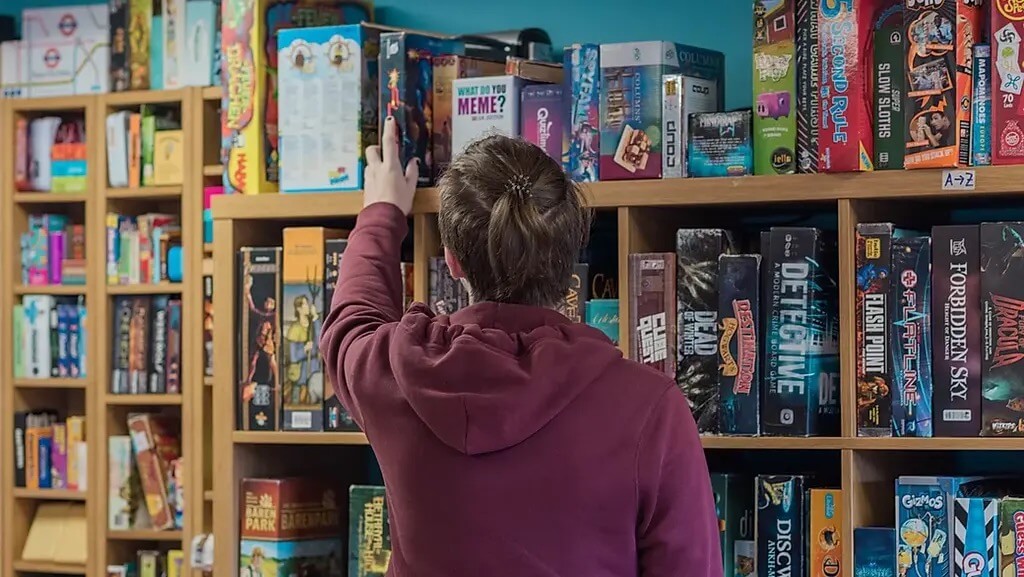 A person selecting a board game from a shelf, enjoying the fun and unique things to do at Sugar and Dice in Liverpool