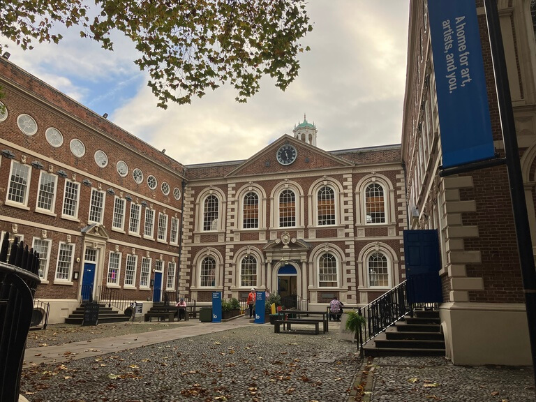 a historic red-brick building with a central courtyard, featuring arched windows and a clock tower, home to the Bluecoat arts centre in Liverpool.