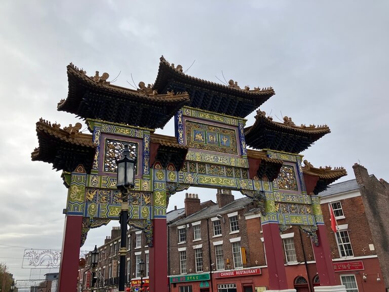 a colourful and intricately designed traditional Chinese arch marking the entrance to Liverpool’s Chinatown, with red pillars and gold detailing.