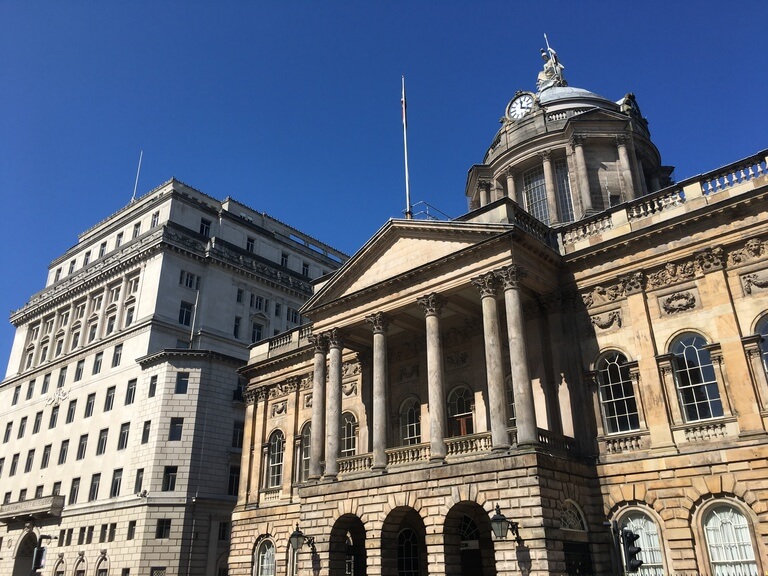 a grand neoclassical building with large columns, a central dome topped with a clock in Liverpool's city centre.